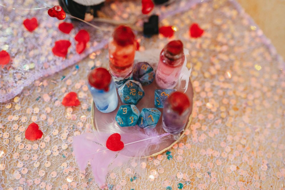 Small red heart decorations and nail polish bottles arranged on a glittery silver surface with soft pink lighting.