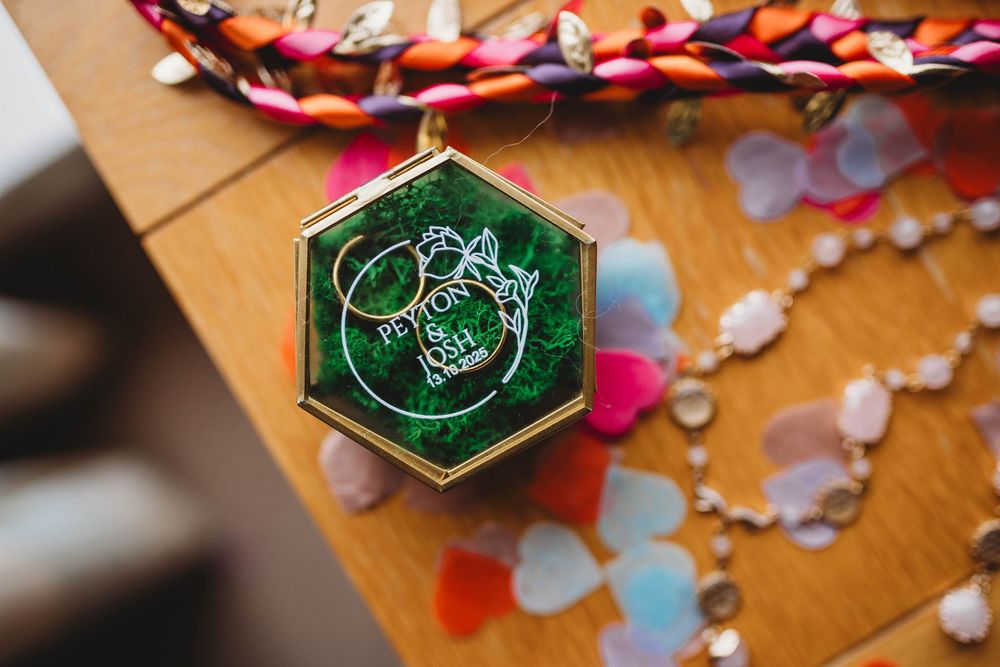 Small green hexagonal box with gold trim sits among scattered rose petals on a wooden surface.