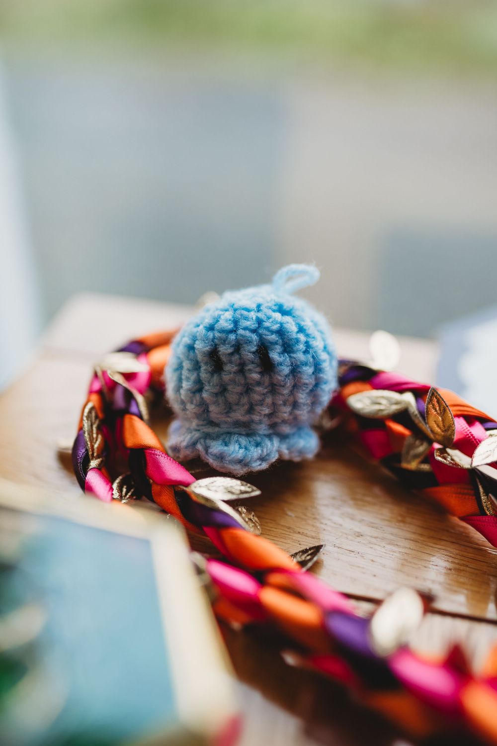 A small crocheted blue ball rests beside a colorful braided fabric on a wooden surface.