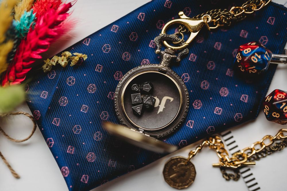 Vintage pocket watch with chain rests on blue patterned fabric next to colorful feathers and decorative items.