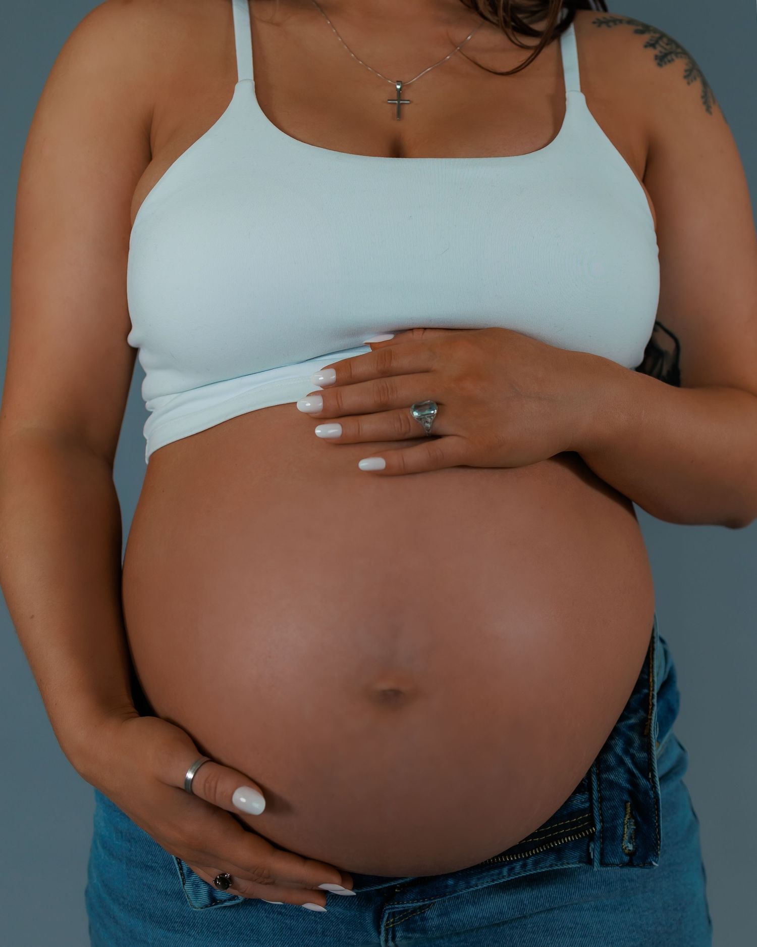 Close-up maternity photograph of a pregnant woman’s hands resting on her belly in a studio setting, highlighting connection and presence dur