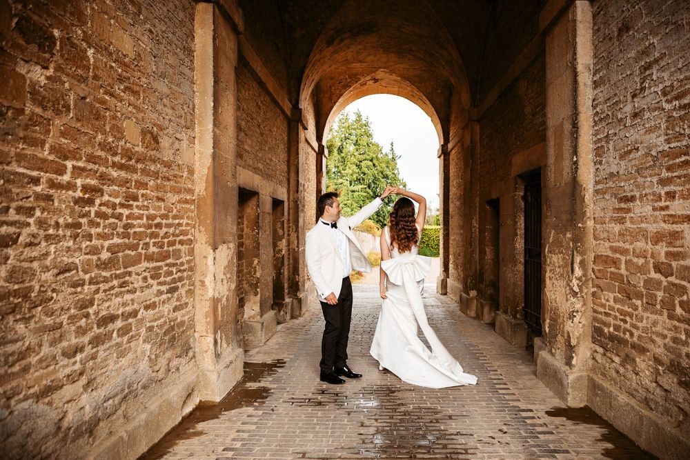 Stone archways line a narrow medieval alley with golden sunlight streaming through in an ancient European town.
