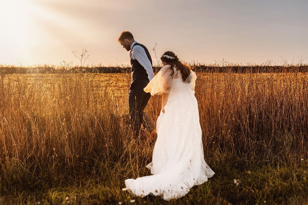 A couple in wedding attire shares a romantic moment in a golden wheat field at sunset.