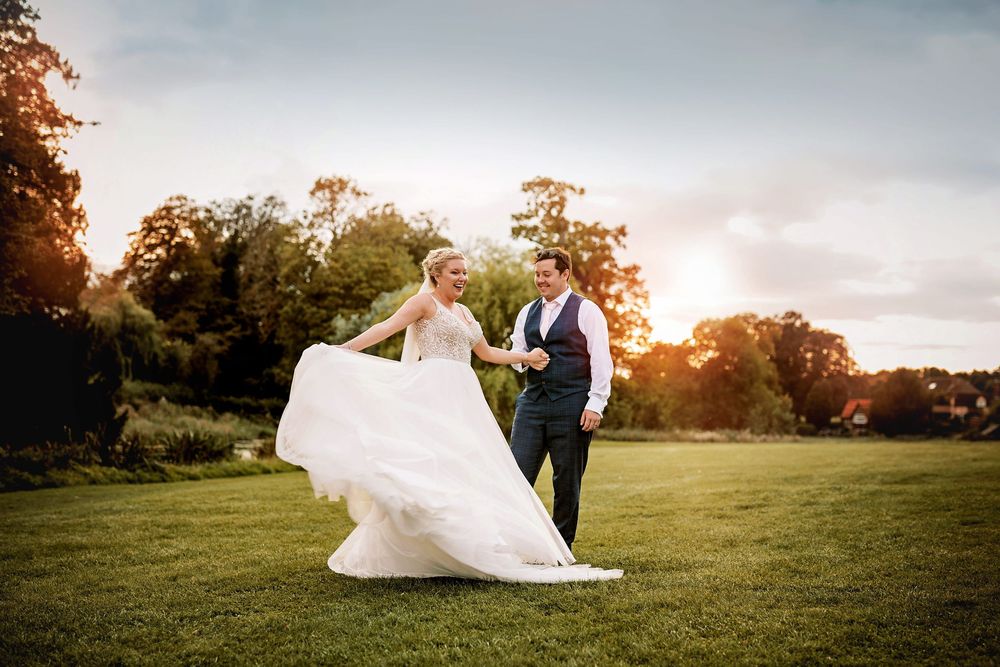 Romantic wedding couple portraits silhouetted against a golden sunset in a grassy meadow with flowing dress details.