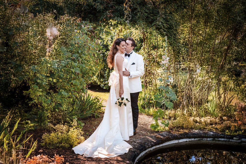 A romantic wedding couple embraces in an enchanted garden setting during golden hour.