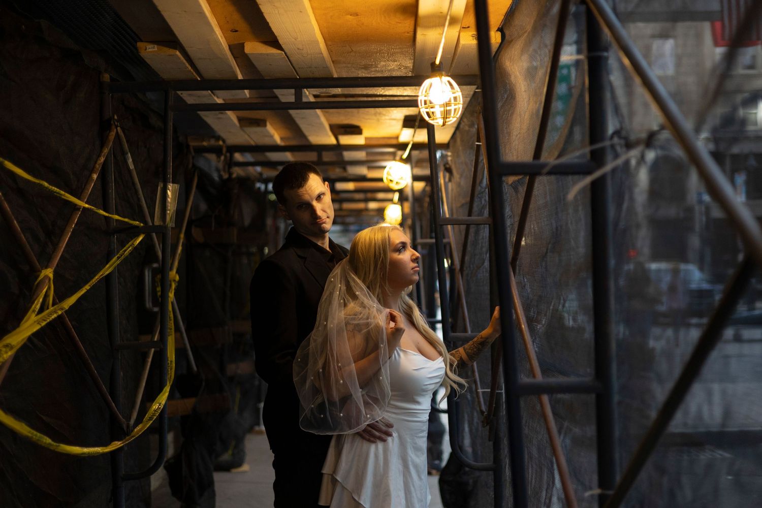 Silhouetted figures stand in a dimly lit industrial space with hanging lights creating a moody atmosphere.