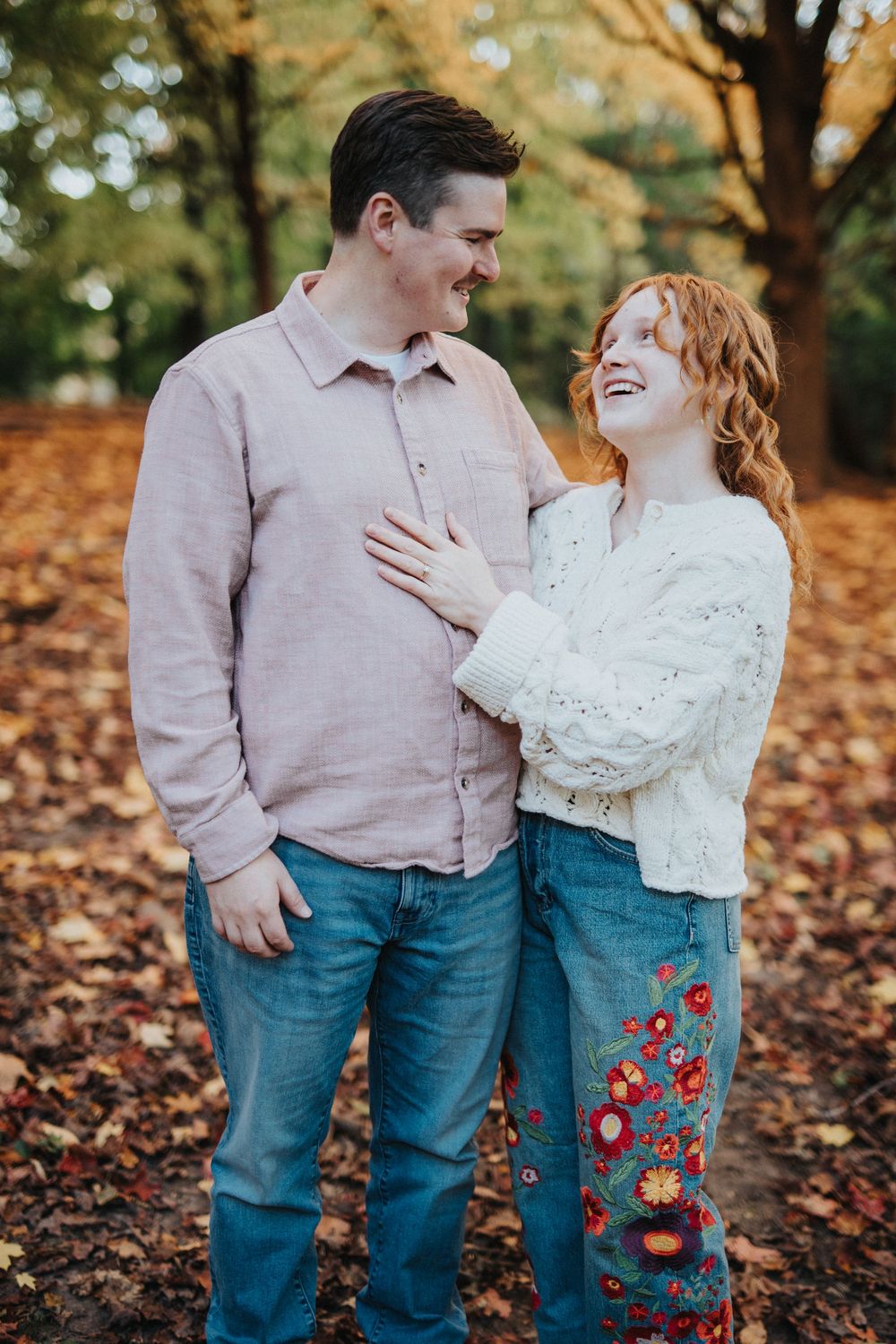 Romantic autumn photoshoot with couple in coordinated outfits among fallen leaves.