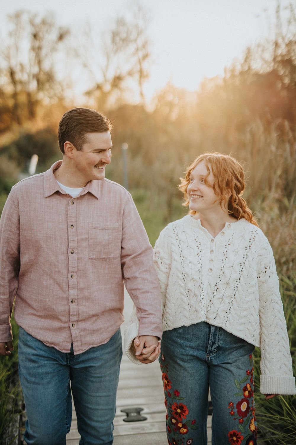 Romantic couple walking hand in hand on a path at sunset wearing coordinated pink and white outfits.