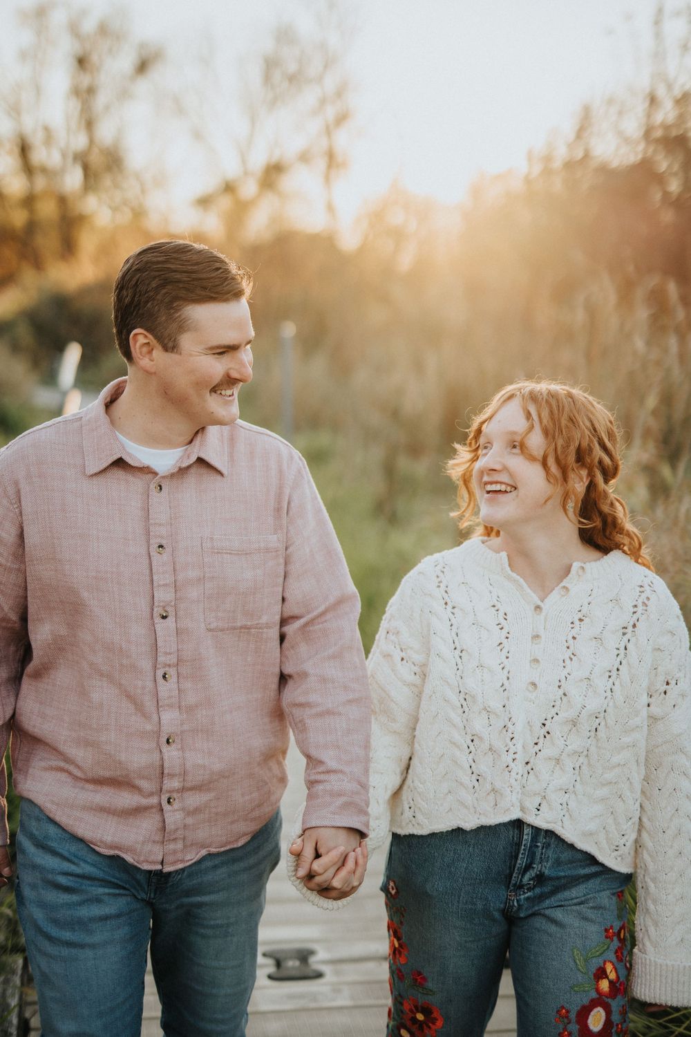 A couple walks hand in hand along a path during sunset, wearing coordinated casual outfits.