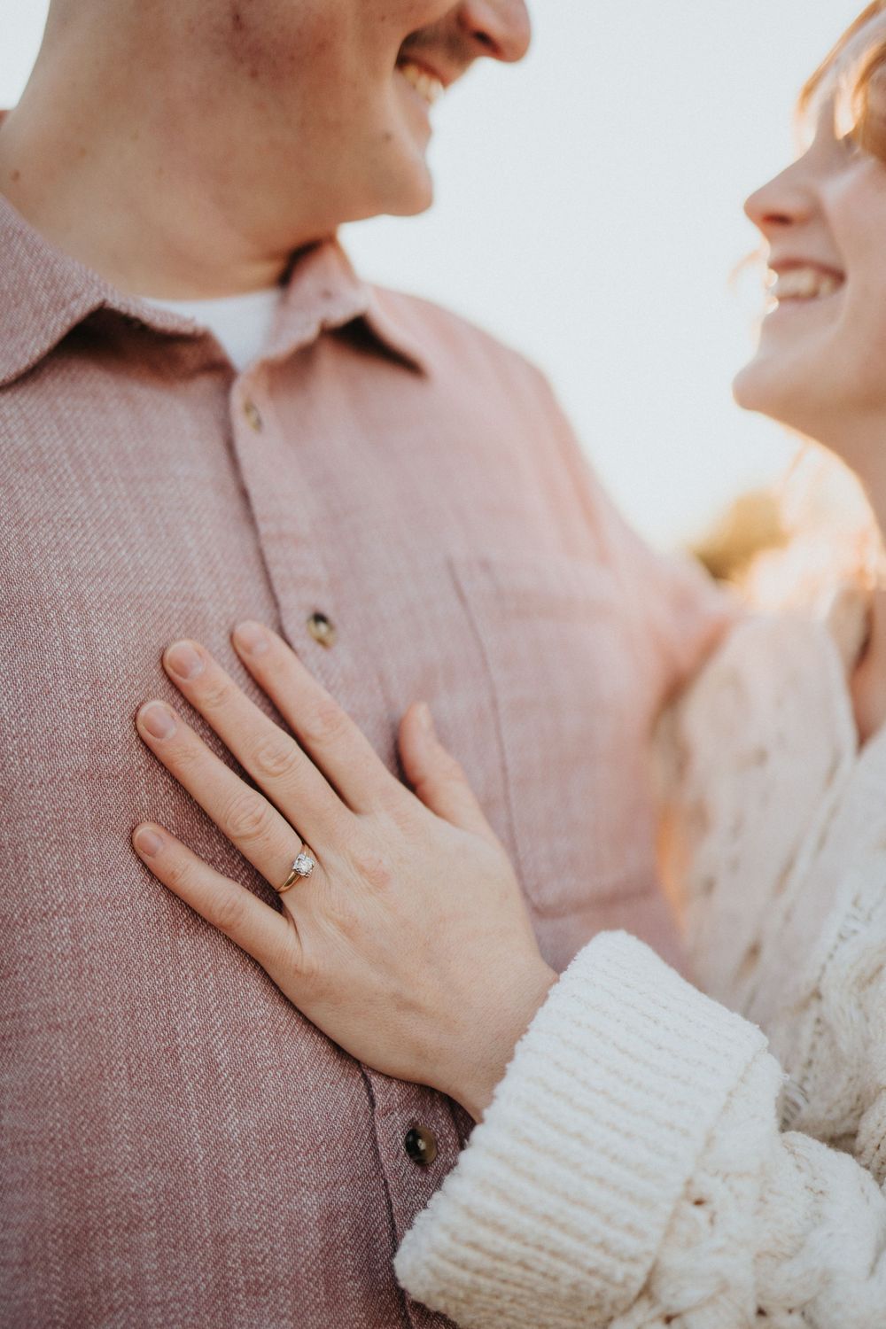 Close-up shot showing hands with an engagement ring against a pink sweater in warm lighting.