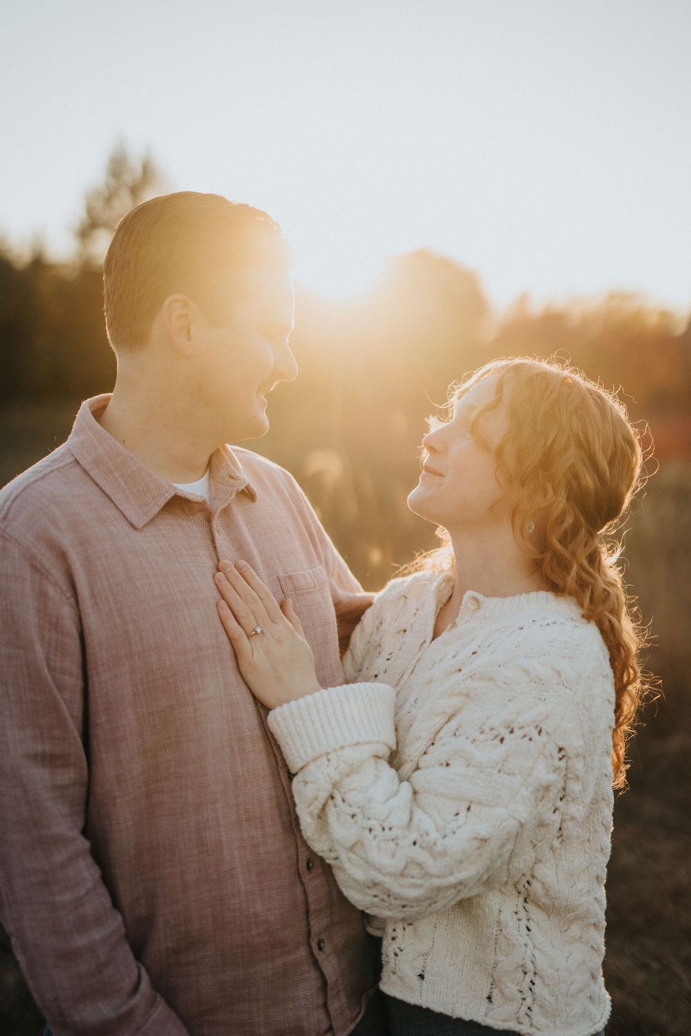 A couple in casual attire shares an intimate moment at sunset with golden light illuminating their silhouettes.
