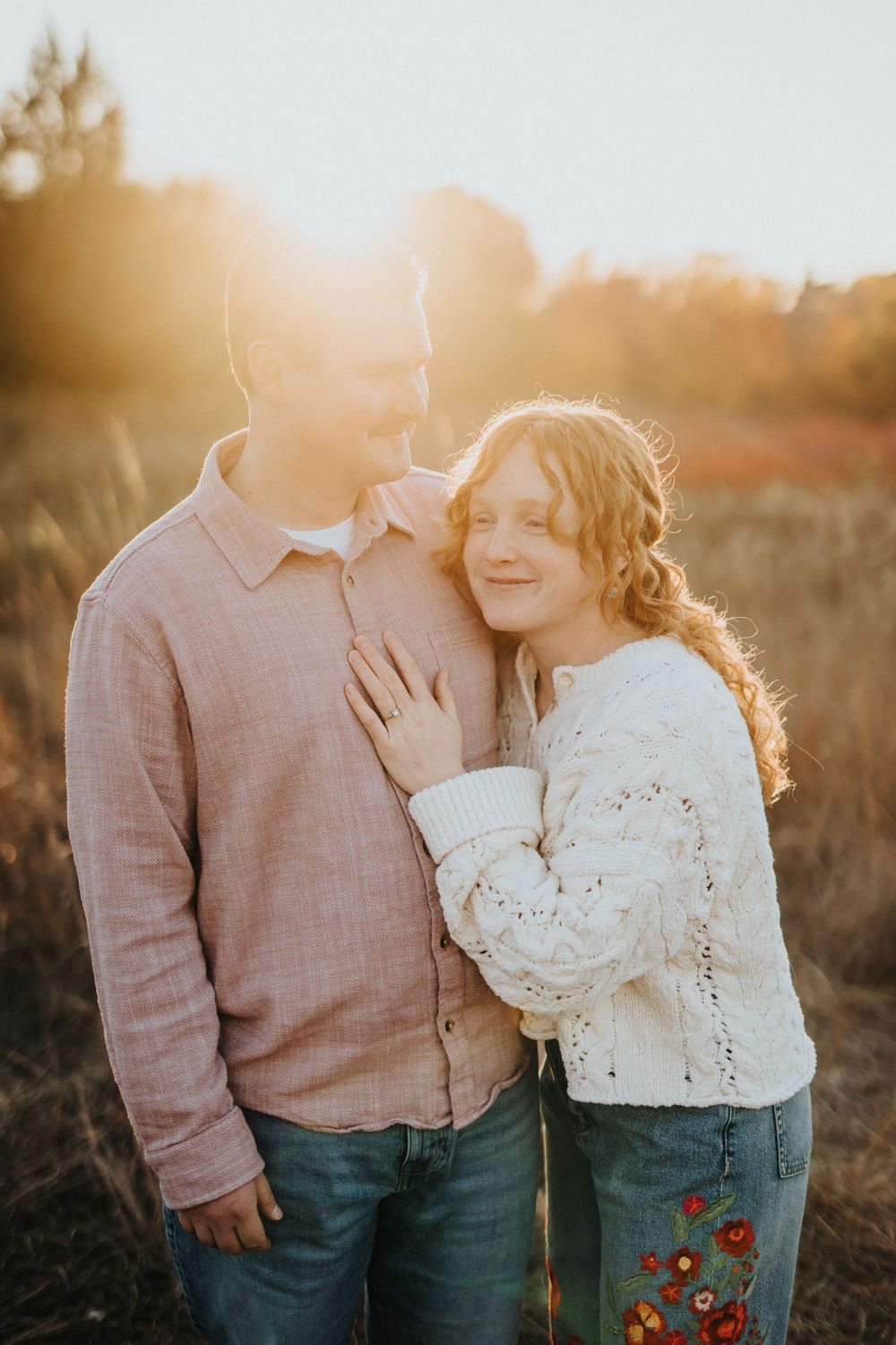 Romantic couple embracing in a field during golden hour sunset wearing pink and white outfits.
