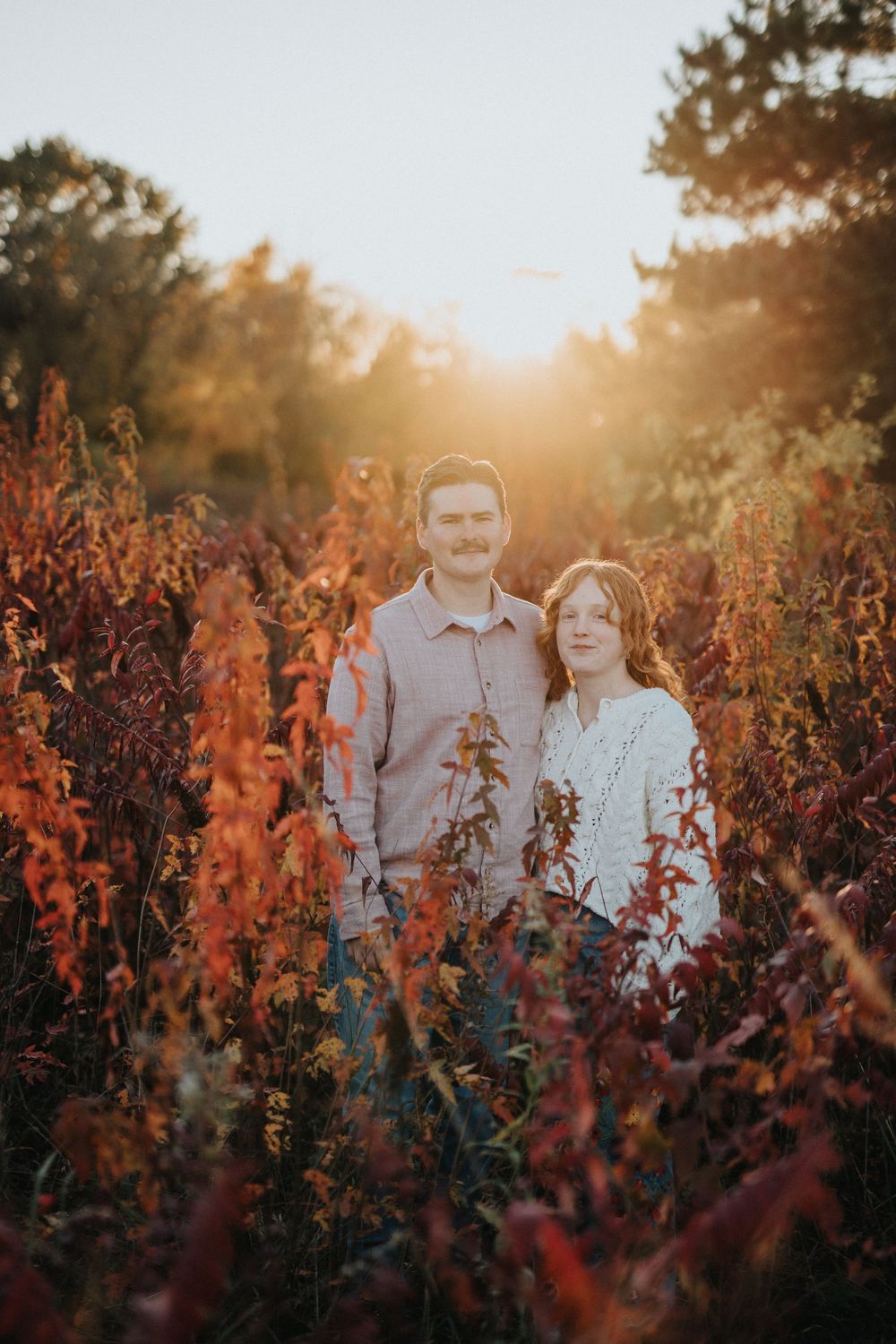 Romantic portrait of a couple surrounded by vibrant red fall plants at sunset.
