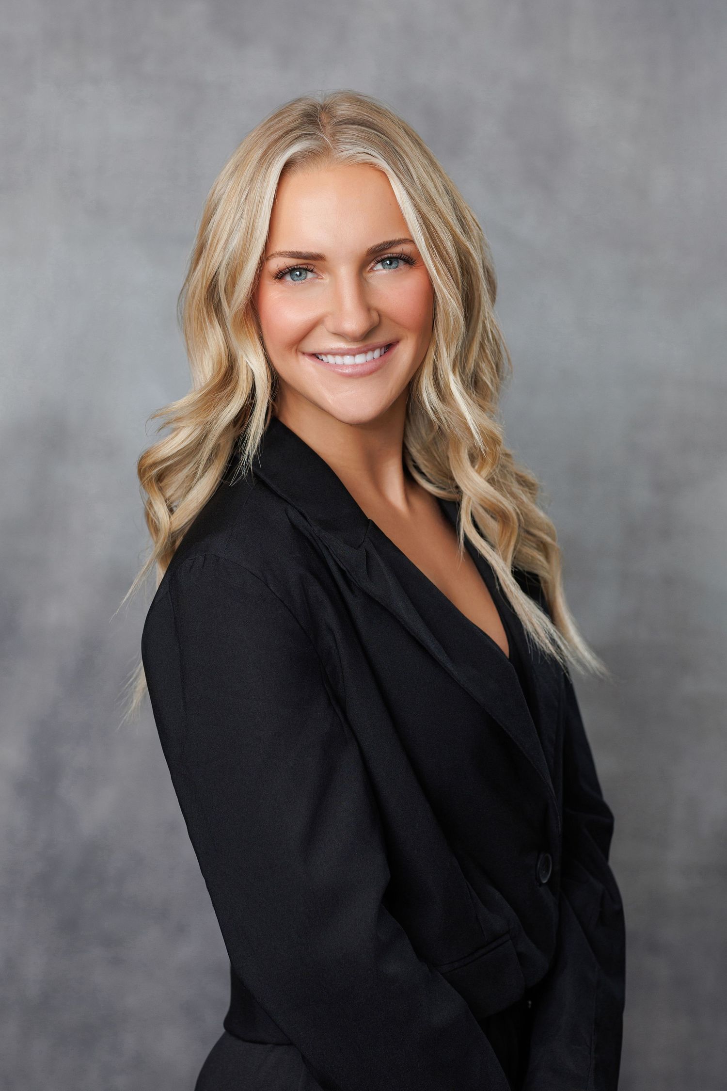 Professional business portrait of person in navy blazer and white blouse standing outdoors in autumn setting.