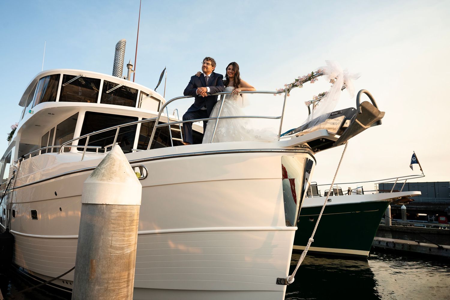 A young newlywed couples stands on the prow of a boat in a harbor in Seattle Washington, celebrating their elopement.