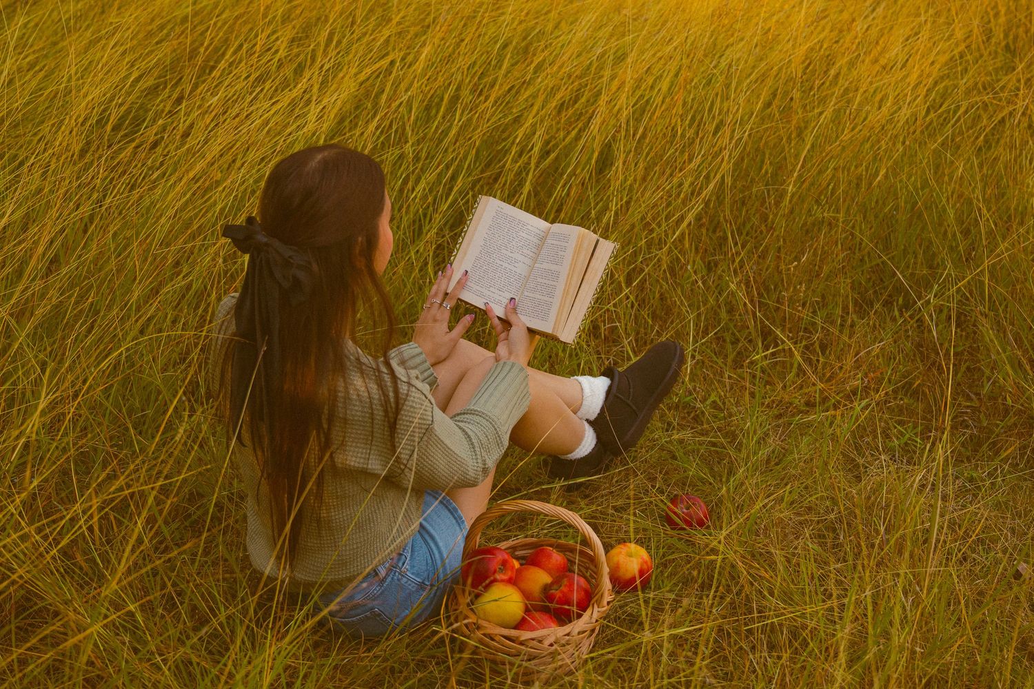 Picnic setup in tall golden grass with blanket and basket at sunset.