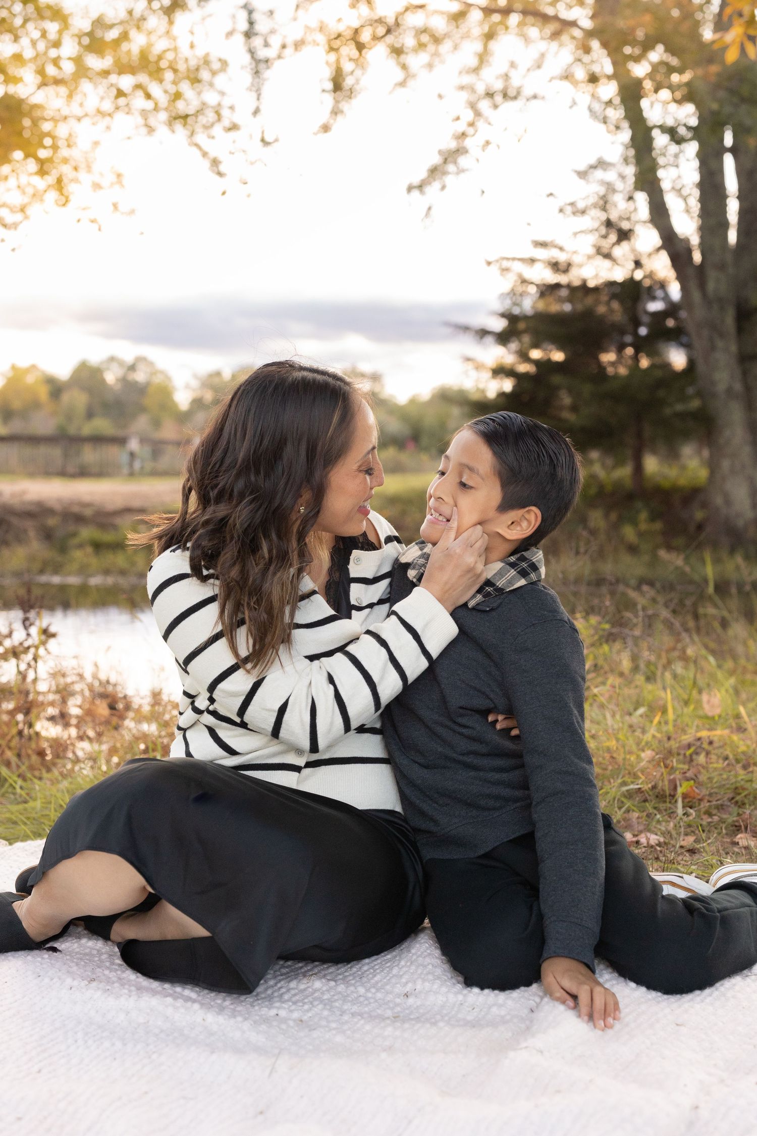 A mother and son sitting on a blanket during sunset sharing a precious moment lake side.