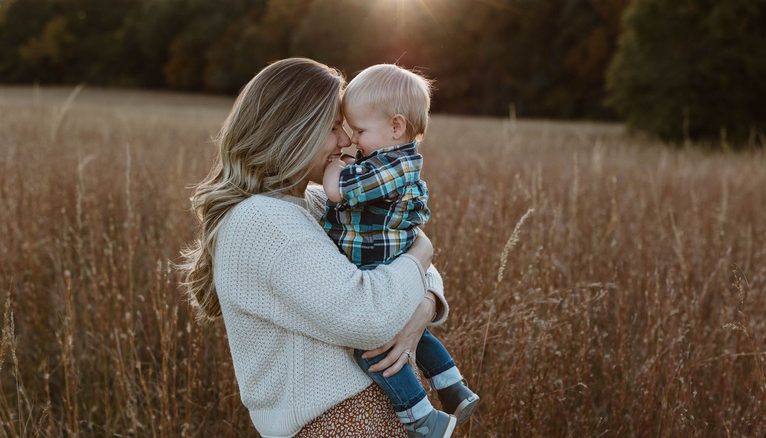 A mother and son shares tender moments in a series of tall grass outdoor photos in a rustic field at golden hour.