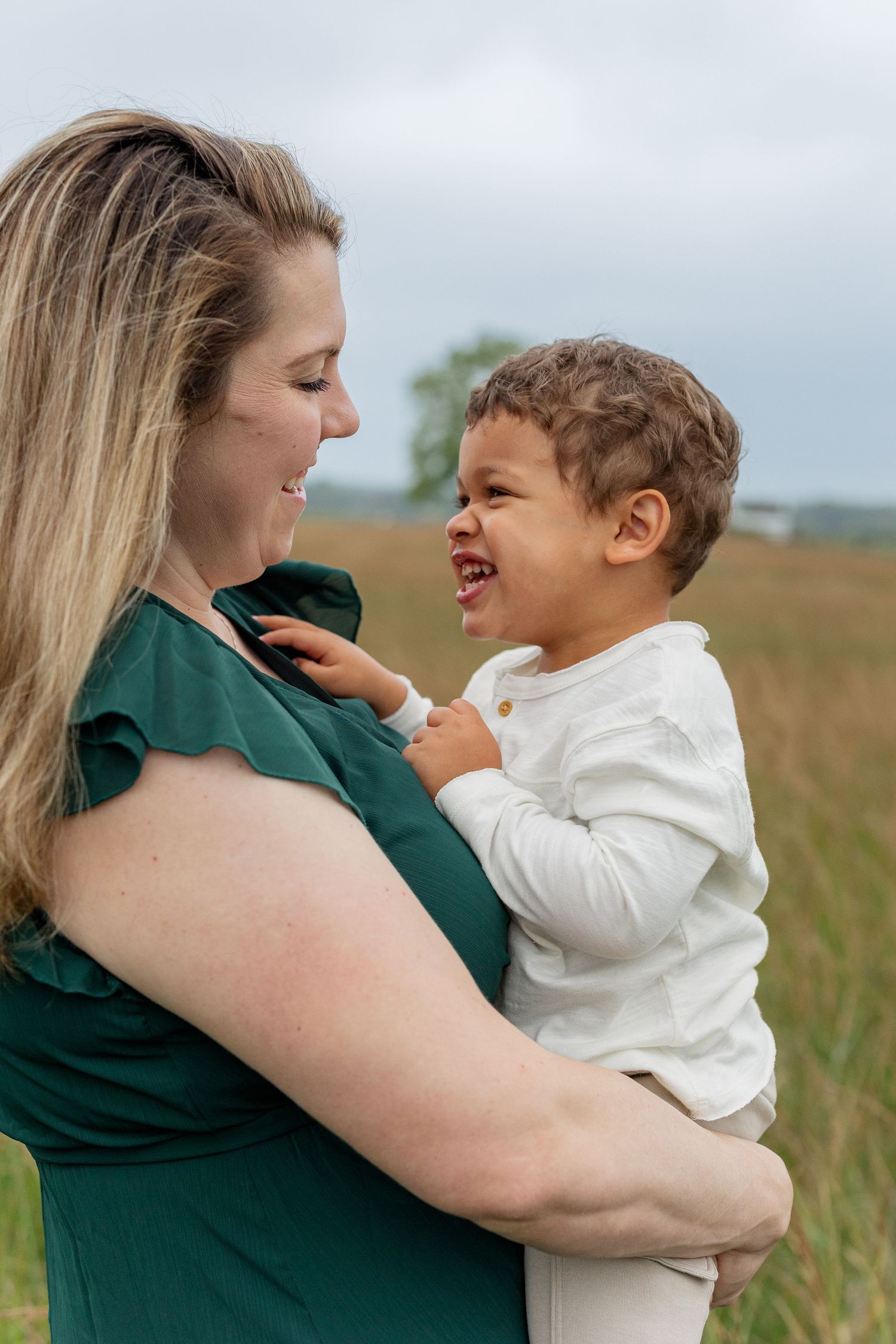 A mother and child share joyful laughter while embracing in a grassy field during a candid photo series.