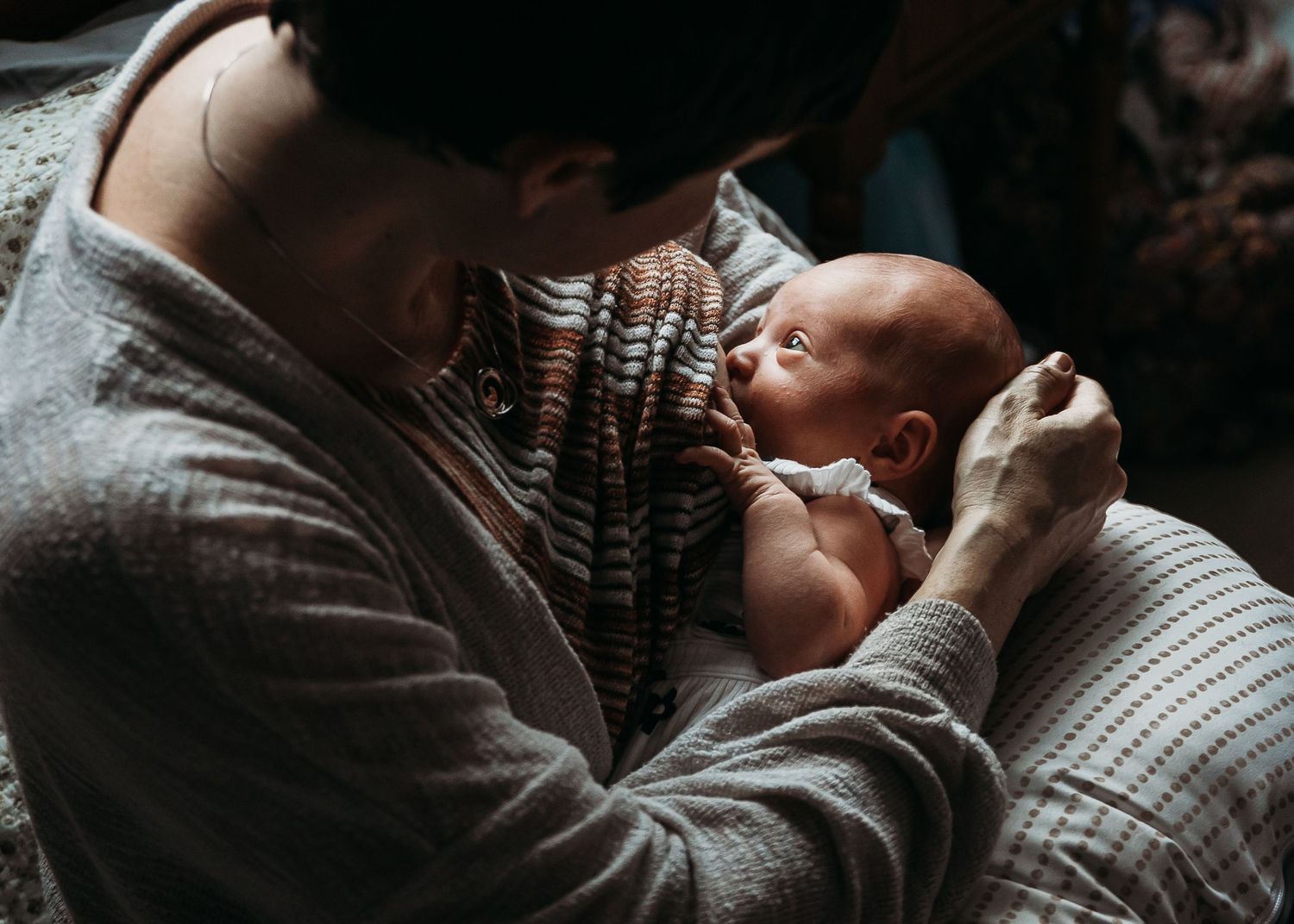 A tender moment between parent and baby in moody lighting against dark background.