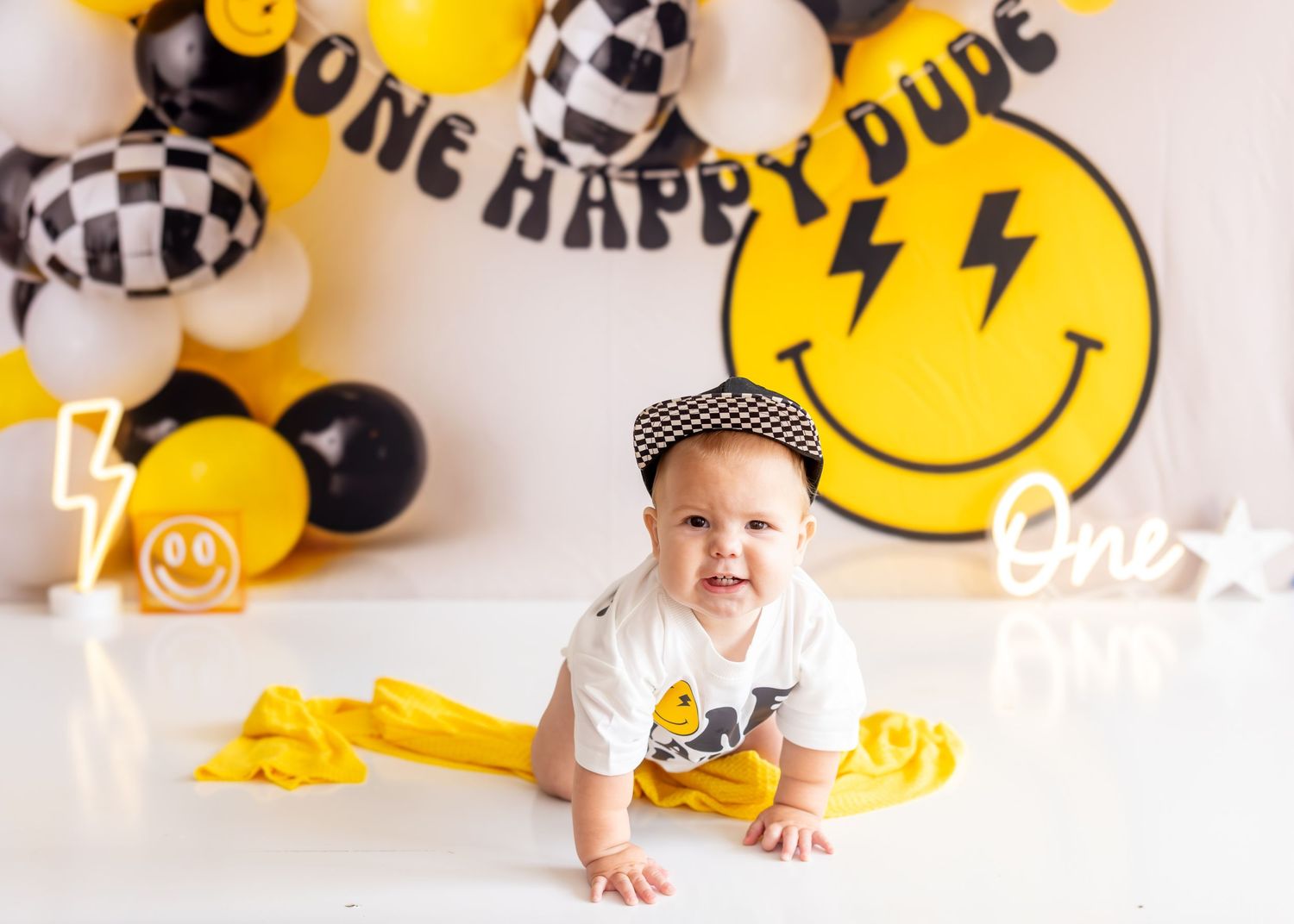 Yellow and black themed birthday party decorations with smiley face balloons and checkered racing flags.
