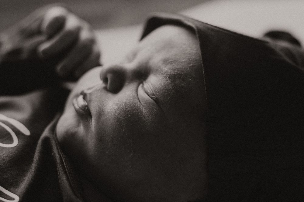 A close-up black and white photograph shows a peaceful baby sleeping in soft bedding.