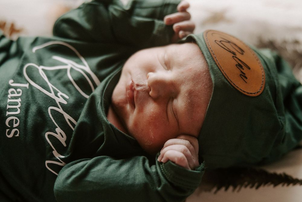 A person wearing a dark green jacket lies down on a wooden surface while looking at the camera.
