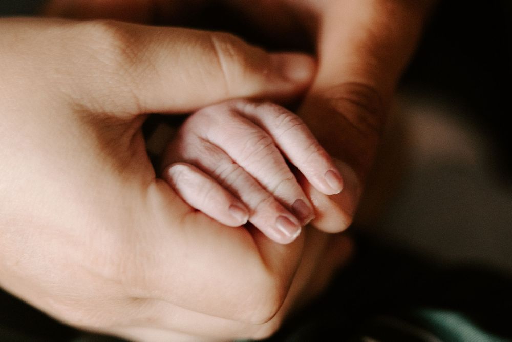 Close-up shot of tiny newborn baby fingers grasping an adult's finger in warm lighting.