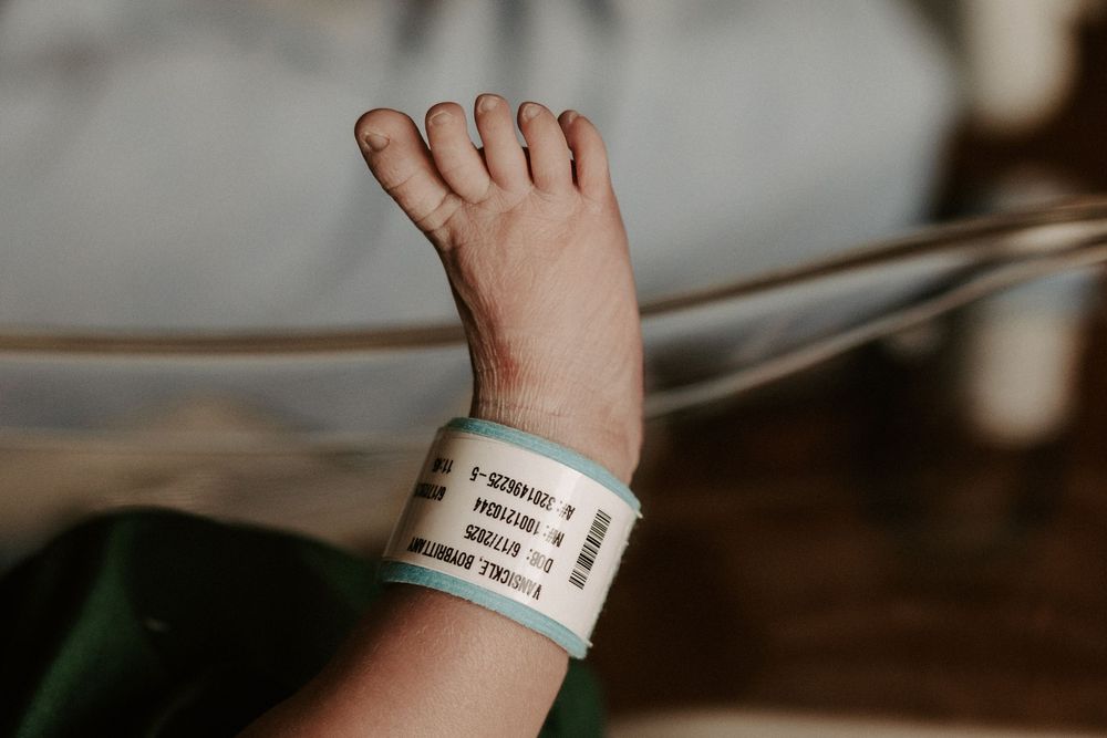 A close-up view of a hospital patient's wristband and hand resting on white bedding.