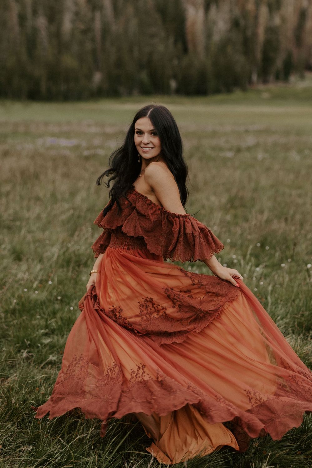 Woman in flowing rust-colored dress twirls gracefully in a grassy meadow during golden hour.