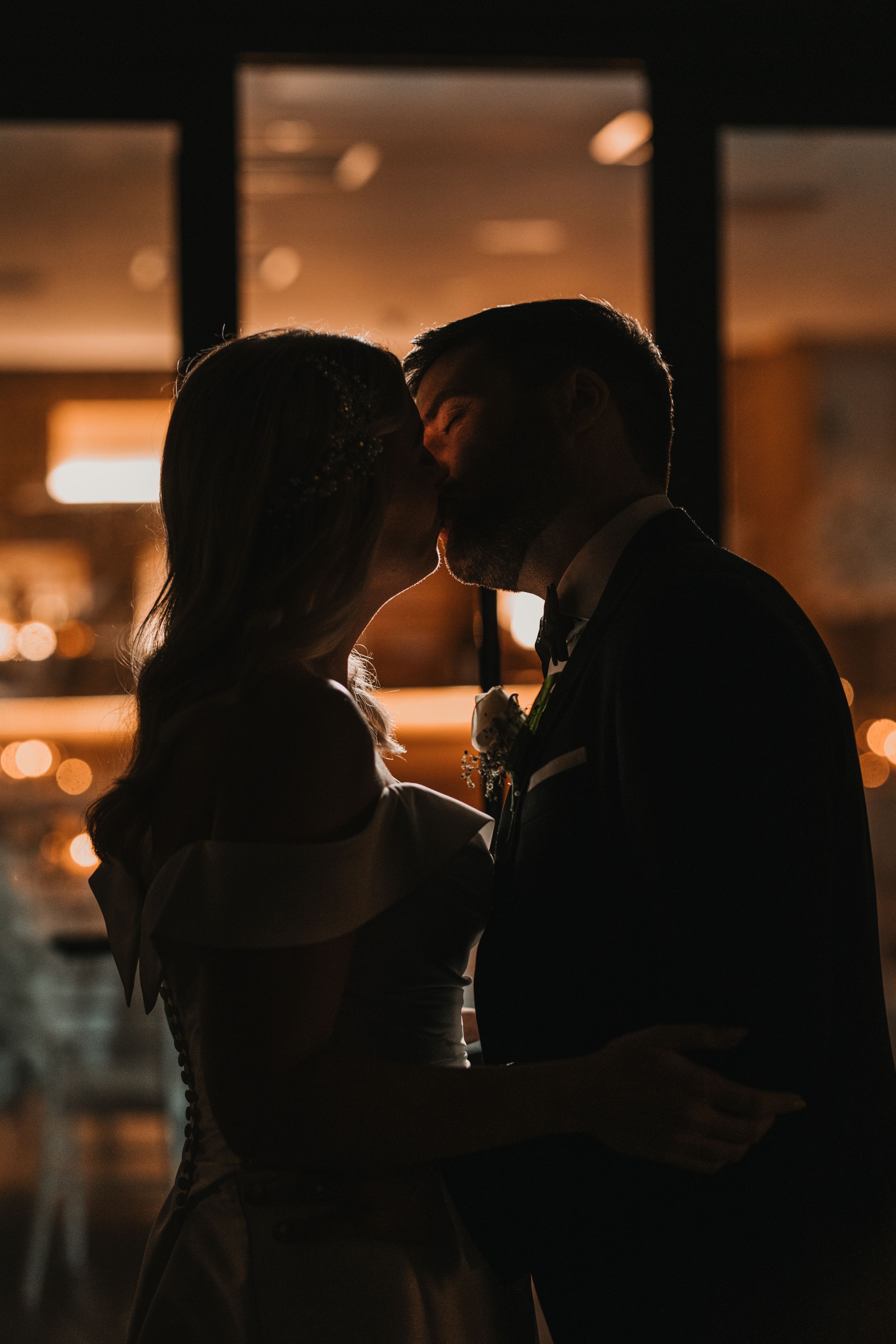A couple share an intimate moment in a warm silhouette against glowing bokeh lights in the background.