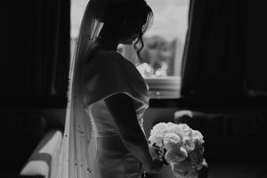 Black and white photo of a bride in silhouette holding a rose bouquet while looking out a window.