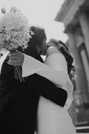 A black and white photo captures a romantic embrace between newlyweds with baby's breath bouquet.