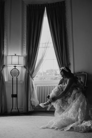A series of five black and white photos showing a figure in a flowing white dress sitting by large windows in an elegant room.