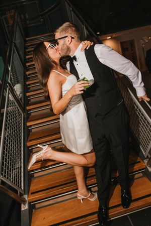 Romantic couple shares intimate kisses on wooden stairs during wedding reception.