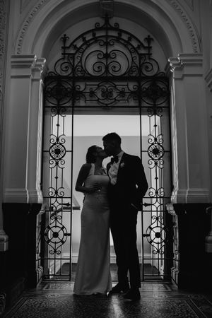 Silhouetted figures stand in ornate archways creating a dramatic black and white wedding scene.