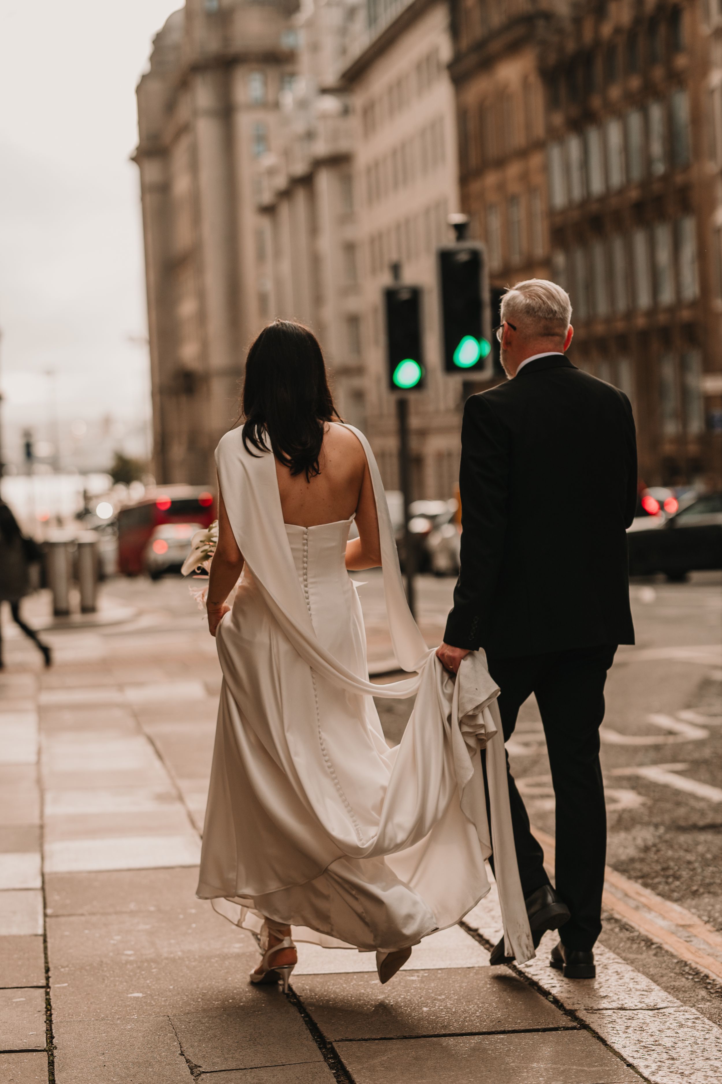 A bride and groom walk together on a cobblestone street in sepia tones with historic buildings in the background.