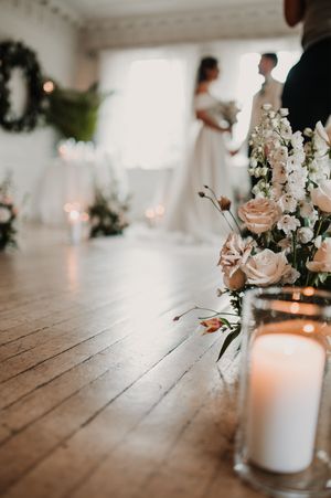 Elegant wedding table decor features white candles and delicate floral arrangements with blush pink blooms on rustic wooden surface.