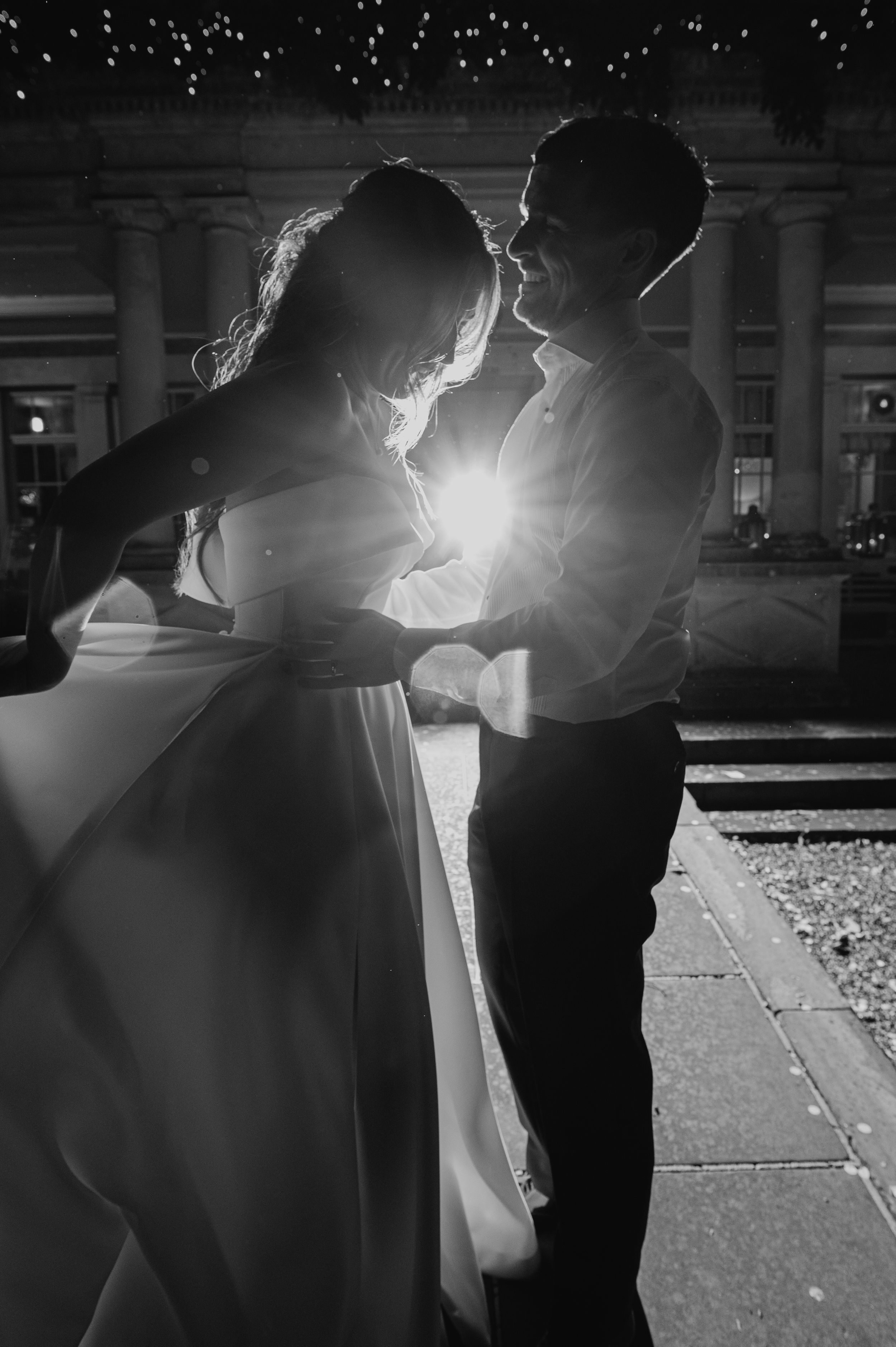 A romantic black and white wedding dance moment backlit by a stunning burst of light.