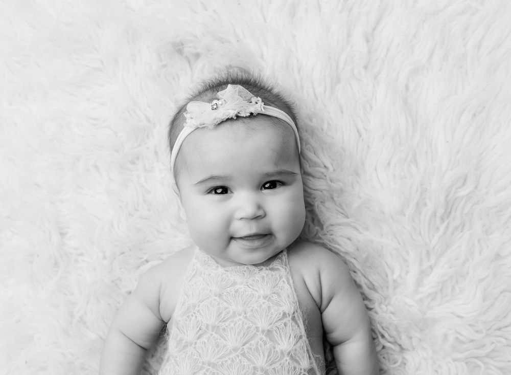 black and white portrait of 3 month baby posed on back smiling at camera on a fluffy flokati rug.