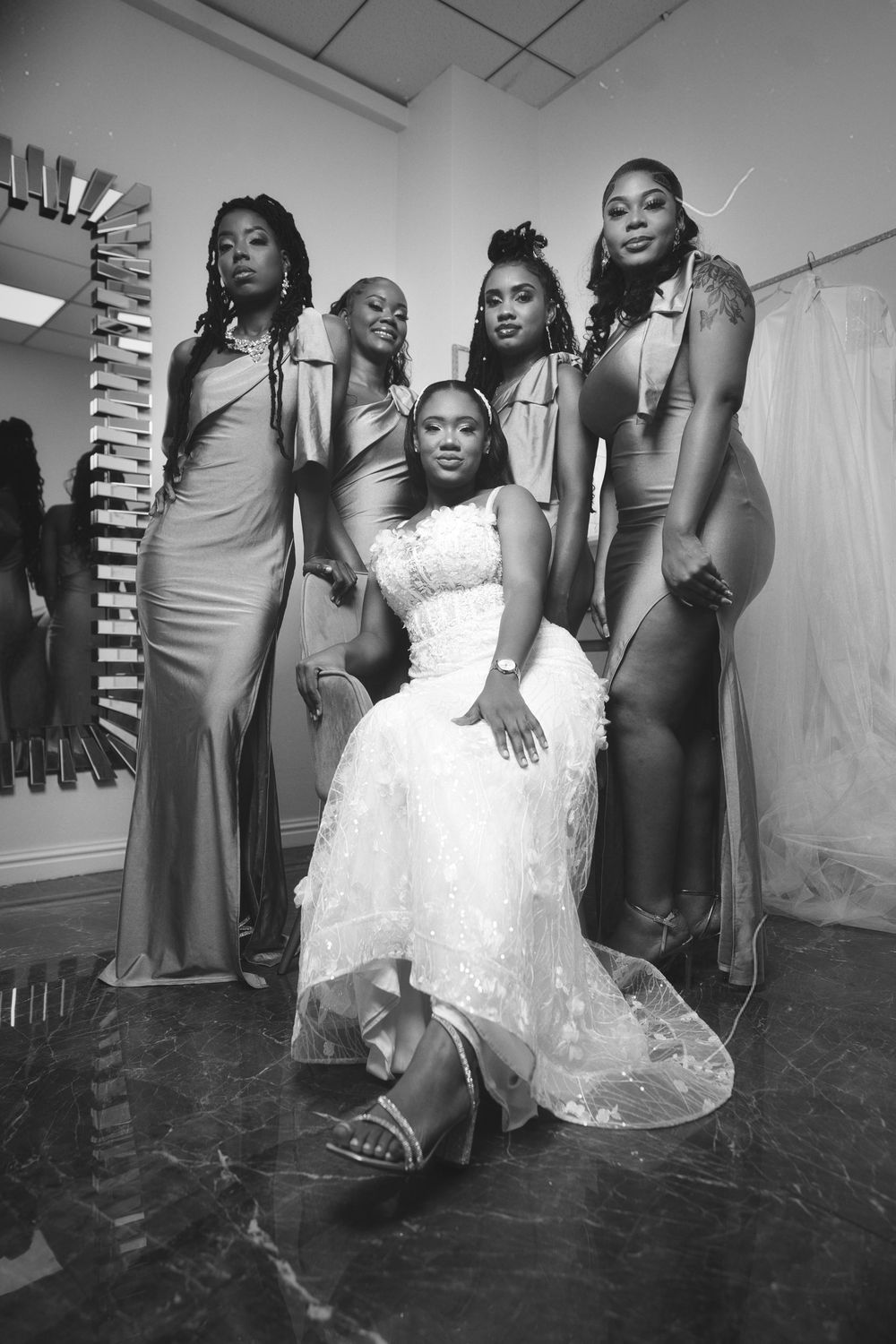 A wedding party in elegant dresses gathers around a bride in a white gown during preparation moments.
