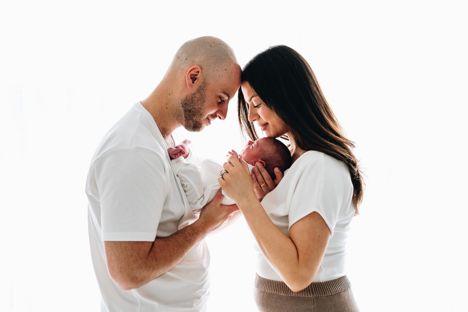 A couple shares an intimate moment with their newborn while leaning their foreheads together taken during a Melbourne newborn photo session.