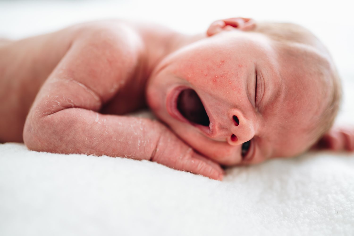 A sleeping baby yawns while resting on soft white bedding taken by Pei Aui a Melbourne local in-home newborn photographer.