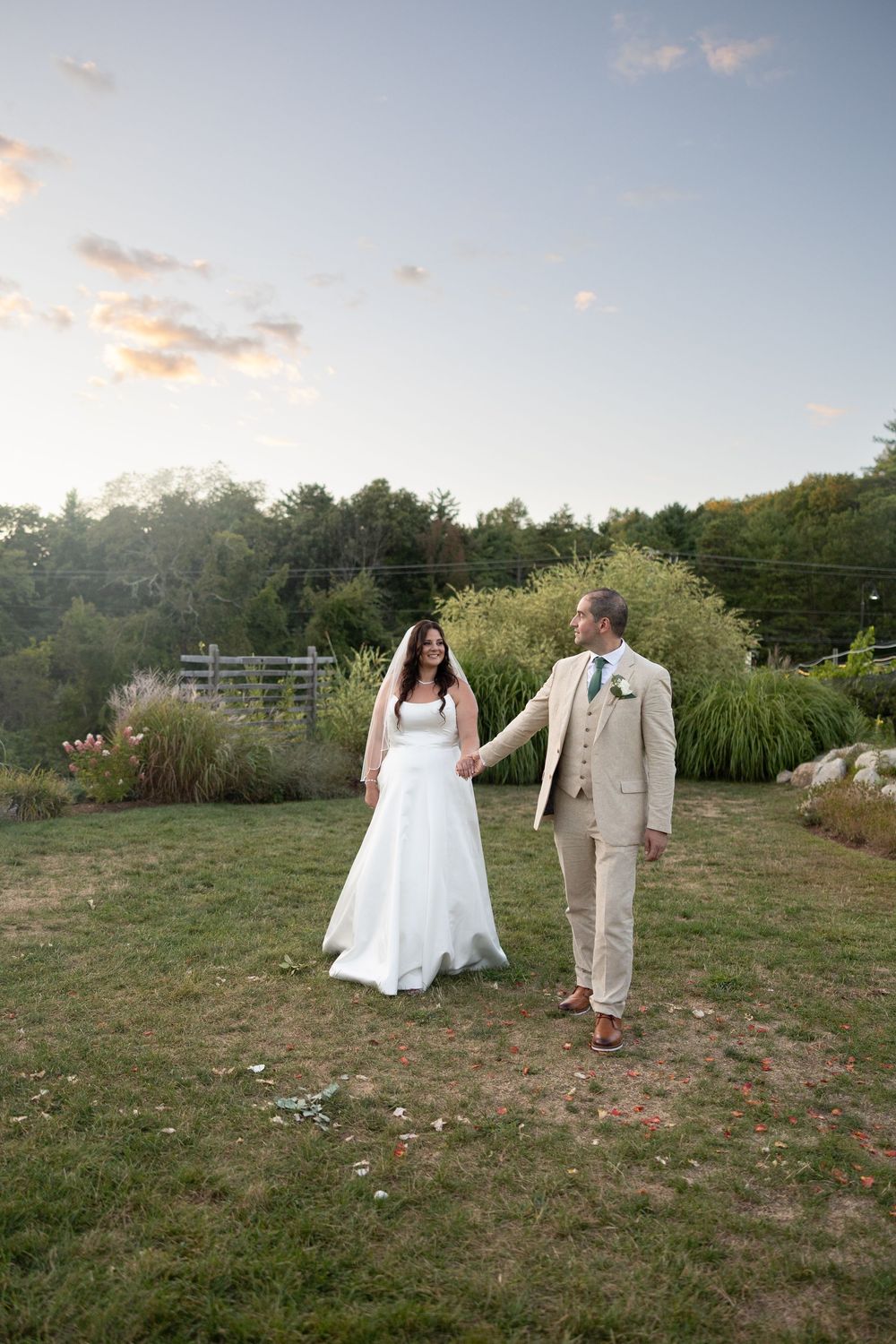 Newlywed couple dances and celebrates in an outdoor field during sunset with trees in the background.
