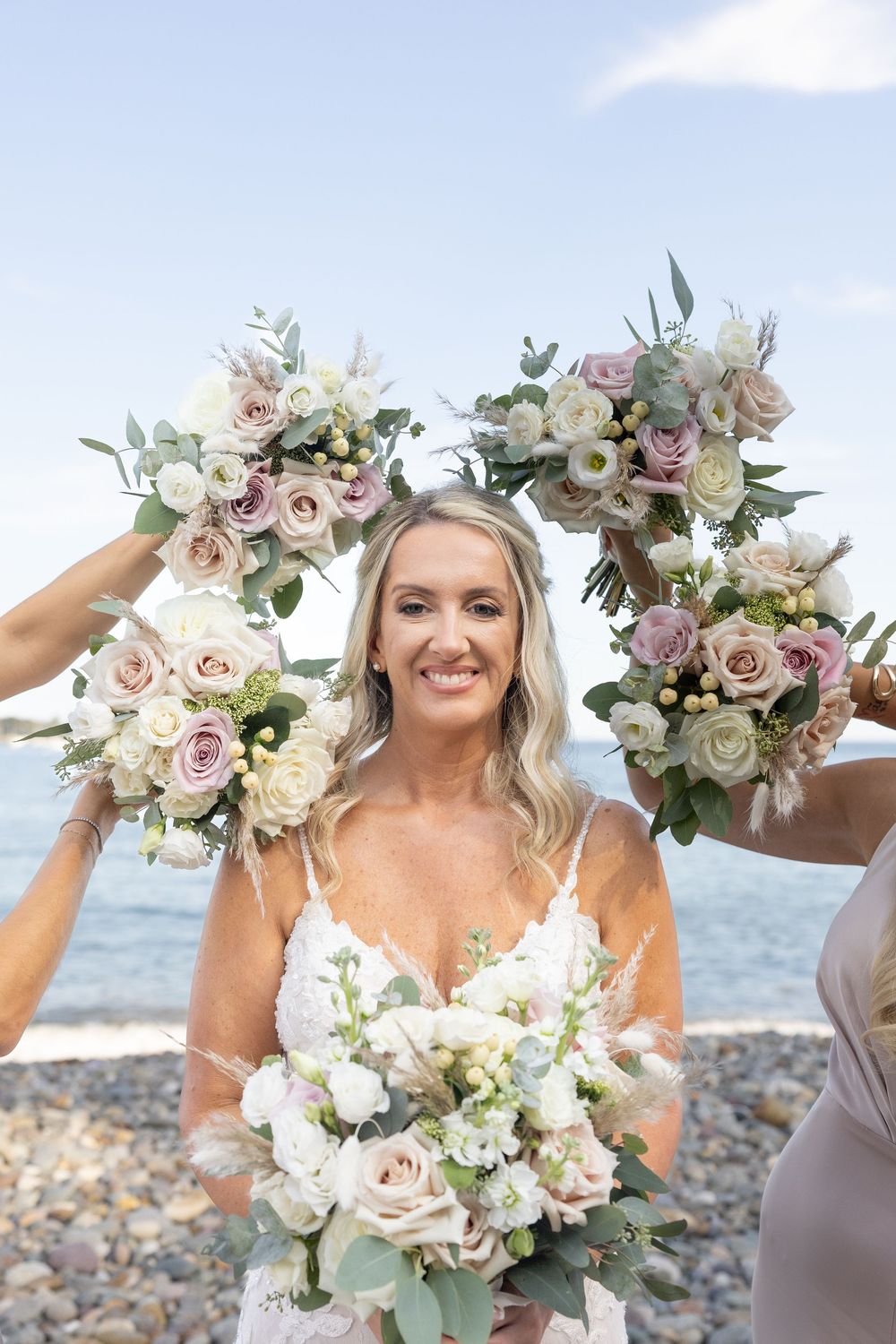 Beautiful bridal bouquet featuring pink roses, white flowers and greenery against an ocean backdrop.