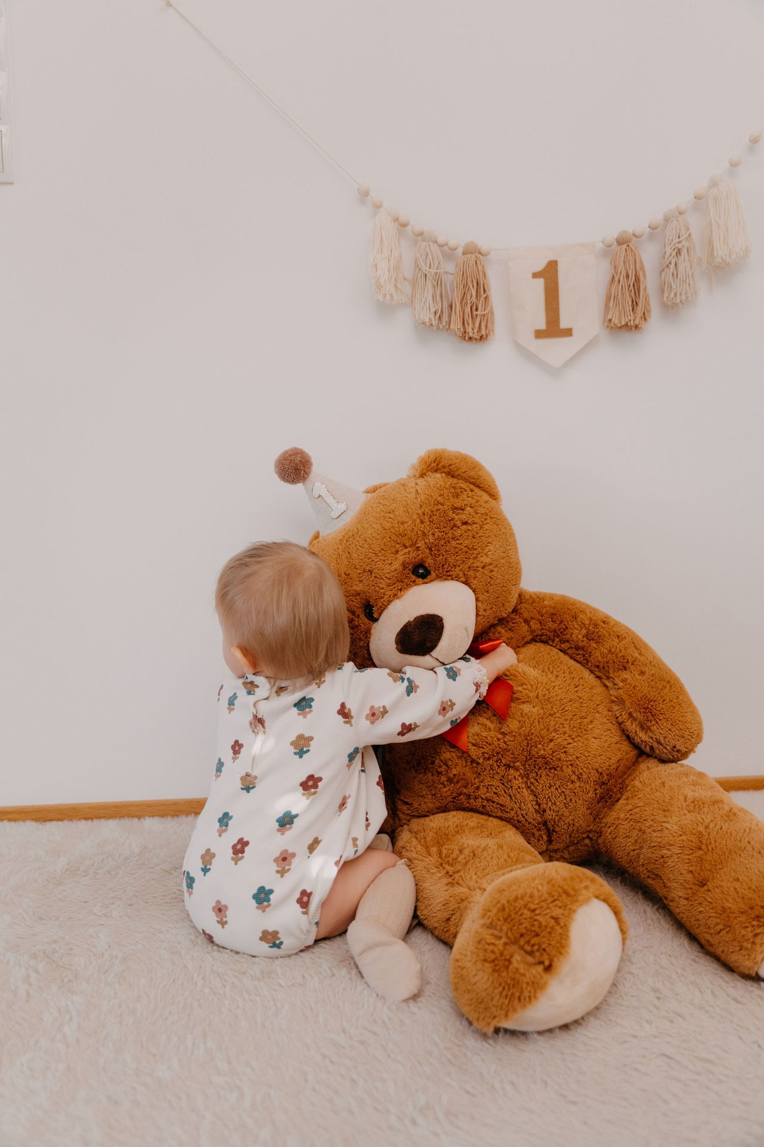 A series of photos showing a toddler in white clothing cuddling with a large brown teddy bear on a light carpet.