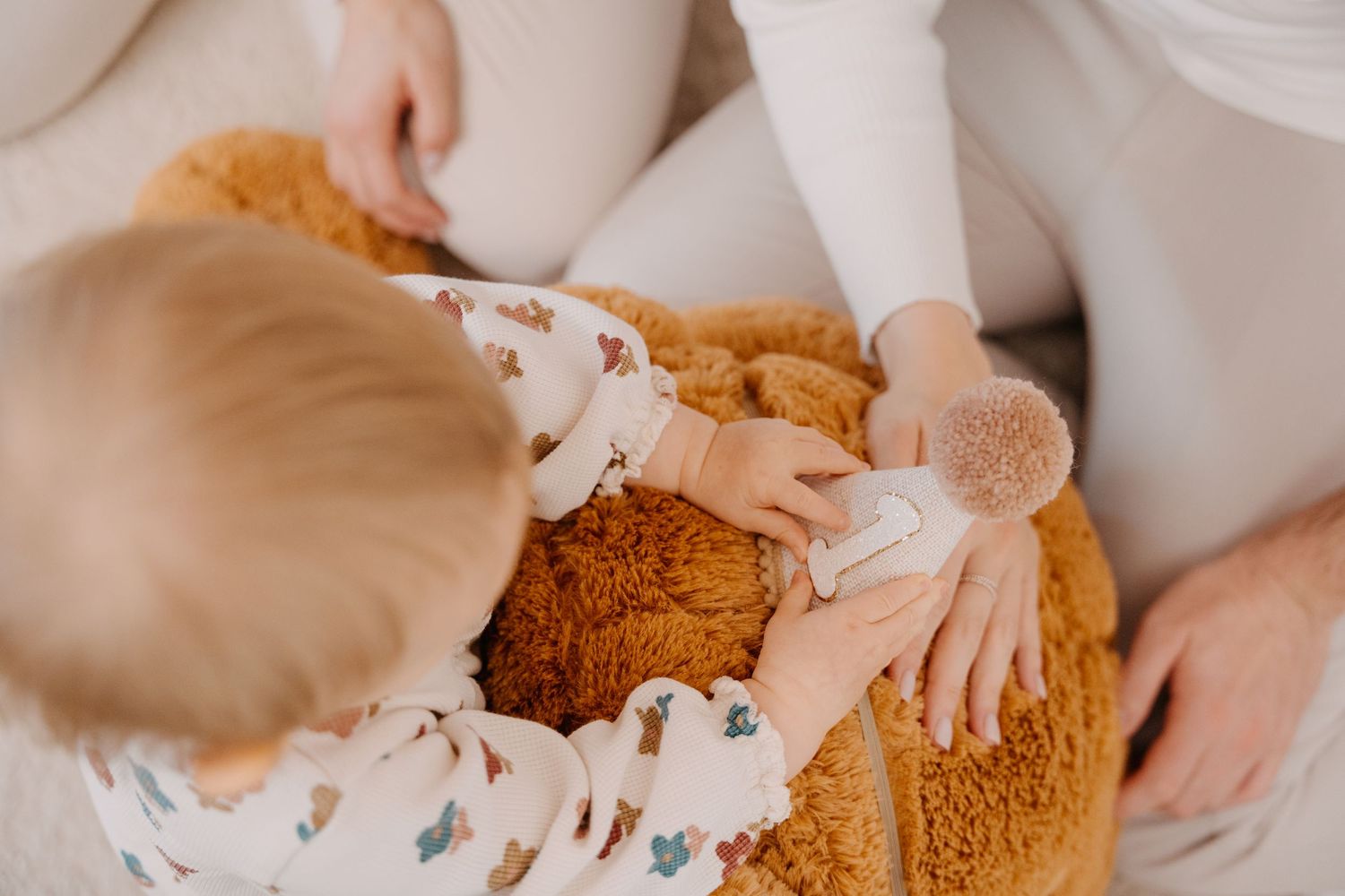 Small hands reach out to touch a large brown teddy bear while wearing floral patterned clothing.