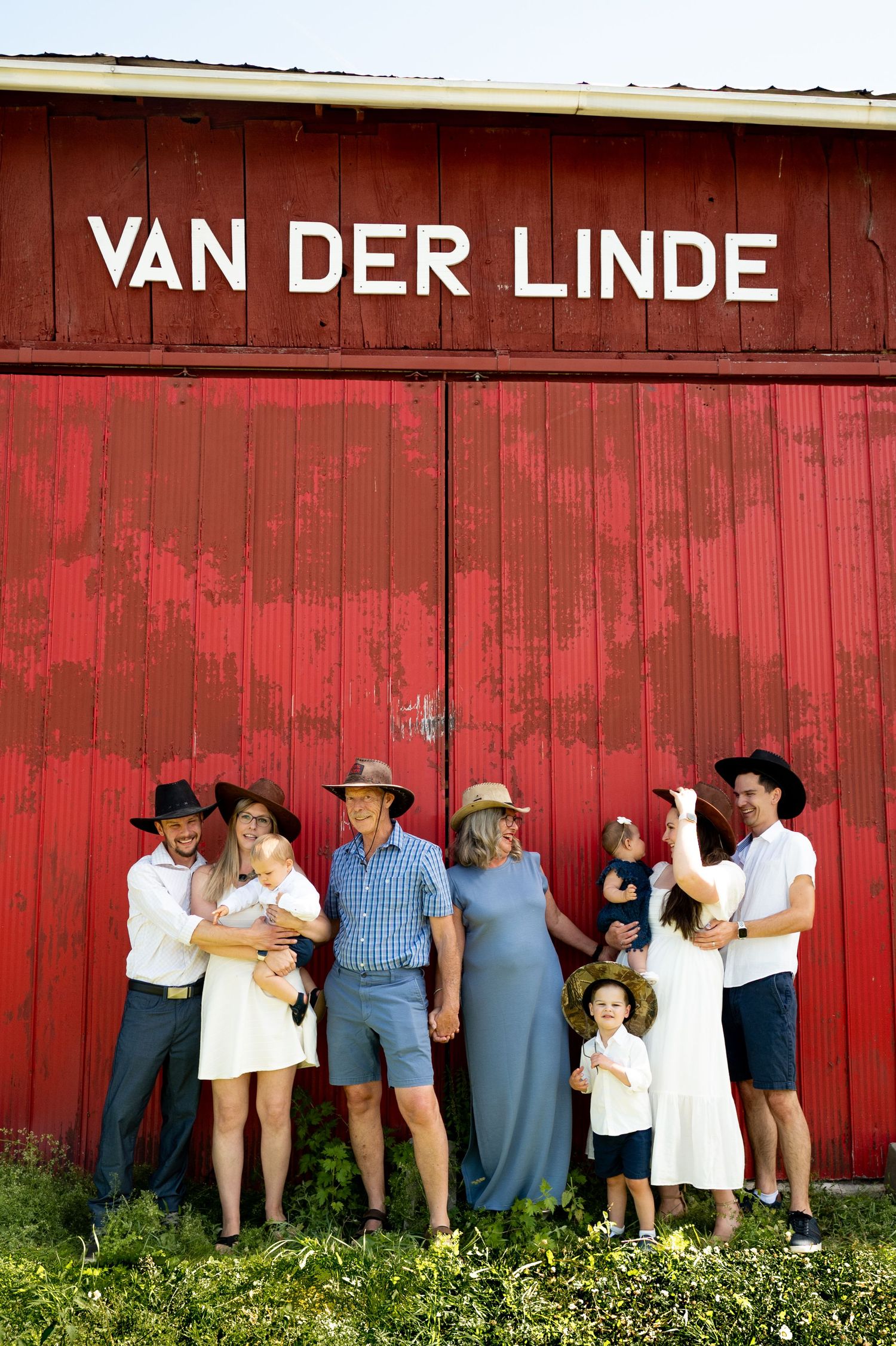 A group of people lined up against a red barn wall in a creative and playful photo series.