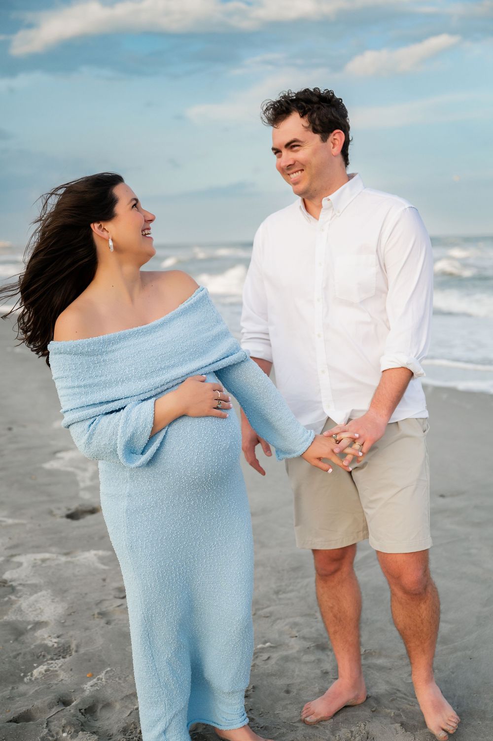 Playful couple's photo session on beach with light blue dress and casual white and khaki attire.