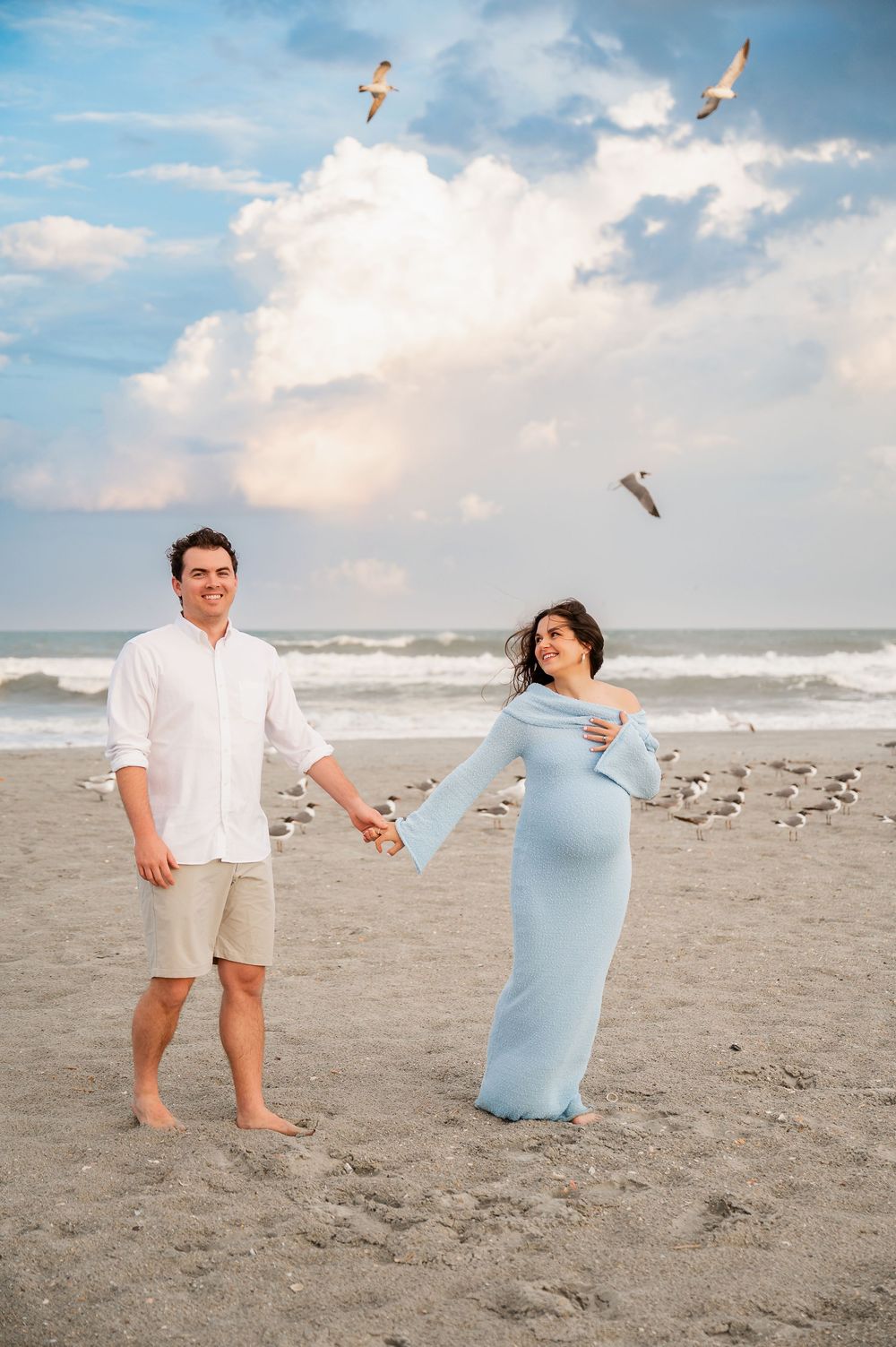 Playful beach photoshoot with couple in light summer attire.